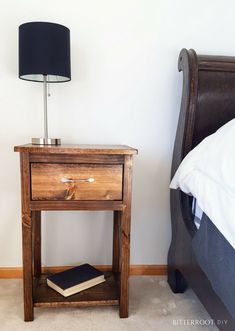 a wooden night stand with a book on it next to a lamp and a bed