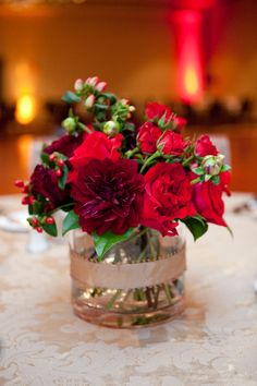 a vase filled with red flowers sitting on top of a white tablecloth covered table