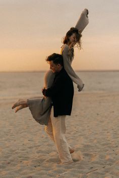 a man carrying a woman on his back while standing on top of a sandy beach