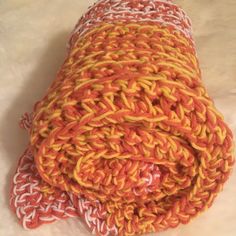 an orange and yellow knitted blanket laying on top of a white tablecloth covered in crochet