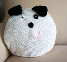 a crocheted white dog pillow sitting on top of a beige couch next to a black nose