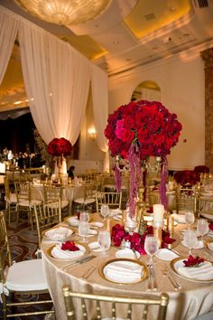 the tables are set with gold chairs and white linens, red flowers in tall vases