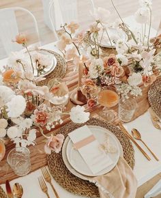 a table set with place settings and flowers in vases, plates, napkins and forks