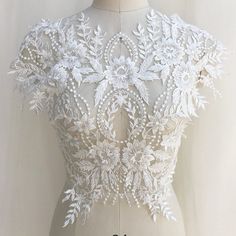 a white wedding dress on a mannequin with flowers and leaves in the back