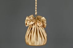 a gold purse hanging from a chain on a gray background with the bottom part of it being held up