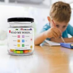 a young boy sitting at a table with a jar of beads in front of him