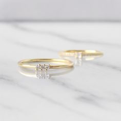 two gold rings with diamonds sitting on top of a white marble countertop next to each other