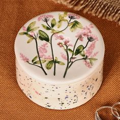 a white box with pink flowers painted on it next to two silver rings and a pair of scissors