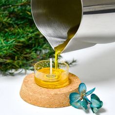 a person pouring olive oil into a small glass bowl on top of a cork coaster