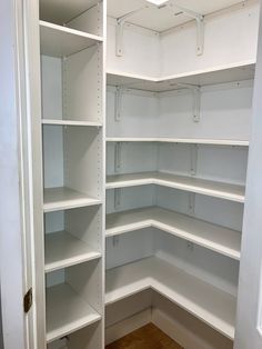 an empty pantry with white shelving and wood flooring in the corner between two doors