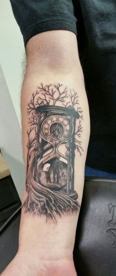 a man's arm with a clock and tree tattoo on the left side of his arm