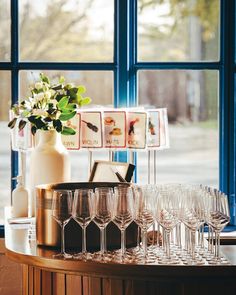 wine glasses are lined up on a table in front of a window with pictures and flowers