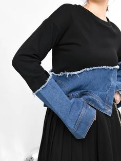 a woman in a black dress is wearing a blue jean jacket with fraying on it