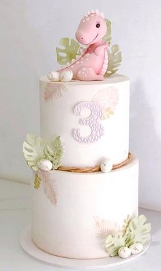 a three tiered cake with a pink dinosaur on top and green leaves around it