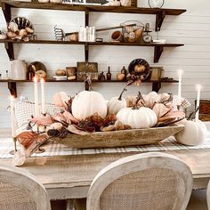 a wooden table topped with lots of white pumpkins and candles on top of it