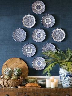 blue and white plates hanging on the wall above a wooden dresser with pineapples