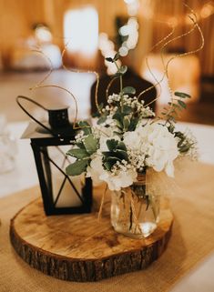 a vase filled with white flowers sitting on top of a wooden table next to a lantern