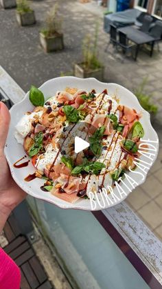 a person holding a white plate with food on it in front of a building window