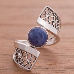 Peruvian artisan Nancy Quispe designs this unique and stunning cocktail ring. A round cabochon of sodalite is framed by a ribbon of sterling silver that wraps around the finger. Attached to that ribbon to complete the ring band are thinner bands of sterling silver that create an open rectangle filled with connected loops of sterling silver worked in the filigree technique. Blue Sodalite, Cabochon Ring, Sterling Silver Filigree, Silver Work, Silver Filigree, Ring Band, Cocktail Ring, Cocktail Rings, Band Rings