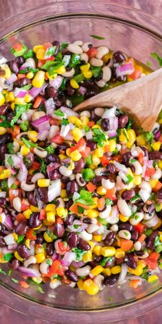 a wooden spoon in a bowl filled with beans and veggies