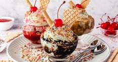 two ice cream sundaes on a white plate with sprinkles and cherries