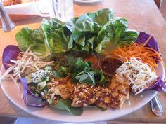 a white plate topped with lettuce, carrots and other food on top of a table