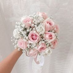 a bride's hand holding a bouquet of pink roses and baby's breath