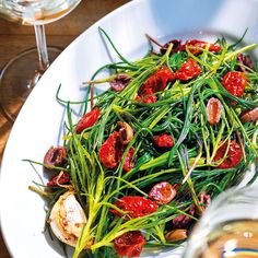 a white plate topped with green vegetables next to a glass of wine