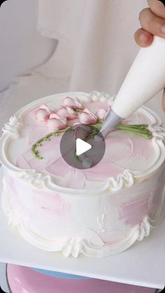 a person is decorating a cake with pink flowers and icing on the top