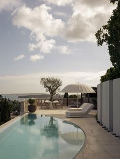 an outdoor swimming pool with lounge chairs and umbrellas on the patio overlooking the ocean