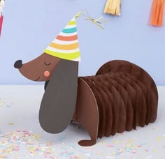 a paper dachshund with a party hat on and confetti in the background