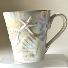 a coffee cup with shells and starfishs on it sitting on a white surface