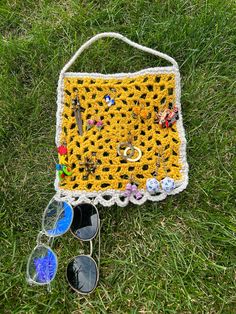 a crocheted purse sitting on top of a grass covered field next to sunglasses