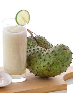 a glass of milk next to a green fruit on a cutting board with a slice of lime