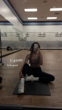 a woman sitting on a yoga mat taking a selfie with her cell phone in an empty room