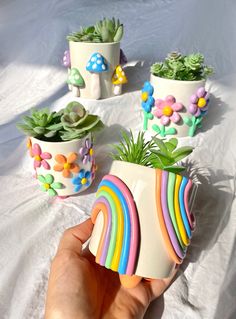 a hand holding a small potted plant with rainbow painted flowers and plants in it