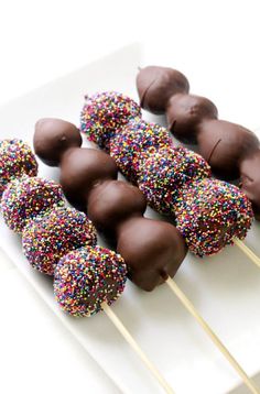 chocolate covered donuts and sprinkles on a white plate with toothpicks