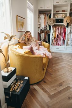 a woman sitting in a yellow chair next to a closet with clothes on the shelves