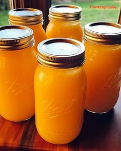 four mason jars filled with orange liquid sitting on a table