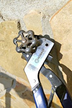 a pair of scissors sitting on top of a piece of metal next to a stone wall