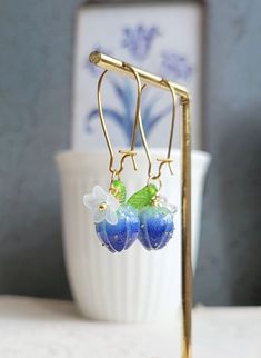 Lovely earrings feature resin blue flower bud adorned with resin small white flower and leaf. On gold plated over brass ear wires.   Total earring length : 42 mm (with ear wire style B) Flower bud size: 10 x 15 mm Purchase over $40 enjoys free shipping! Coupon code 'freeshipping1'. Free Gift Wrapping on request - All items that are gift wrapped come in with a kraft box with raffia string and blank writing card.  Please leave a note if you need it upon ordering. Delicate Blue Flower Earrings With Ear Wire, Resin Flower Charm Drop Earrings, Blue Flower-shaped Resin Earrings, Flower Bridesmaid, Chinese Accessories, Small White Flowers, Rose Bud, Earrings Flower, Bridesmaid Flowers