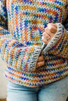 a woman wearing a multicolored sweater with her hands on her hip and holding onto the sleeves