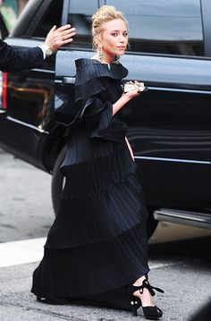 a woman in a long black dress is walking down the street with her hand out