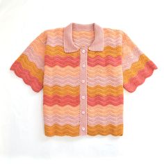 an orange, pink and yellow knitted cardigan with buttons on the collar is laying on a white surface