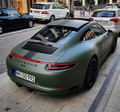 there is a green porsche parked on the side of the street in front of other cars