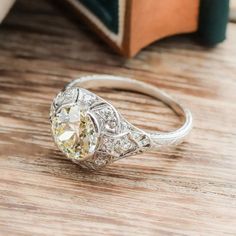 a fancy ring with an oval cut diamond in the center sits on a table next to a book