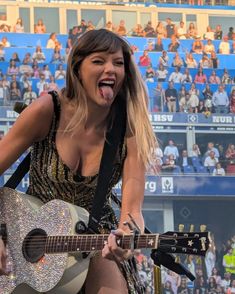 a woman with her mouth open holding a guitar and singing into the microphone in front of an audience