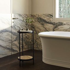 a white bathtub sitting next to a window in a bathroom with marble walls and floors