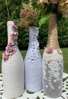 three vases with flowers in them sitting on a white table outside near some bushes