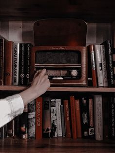 a person is reaching for an old radio on a book shelf